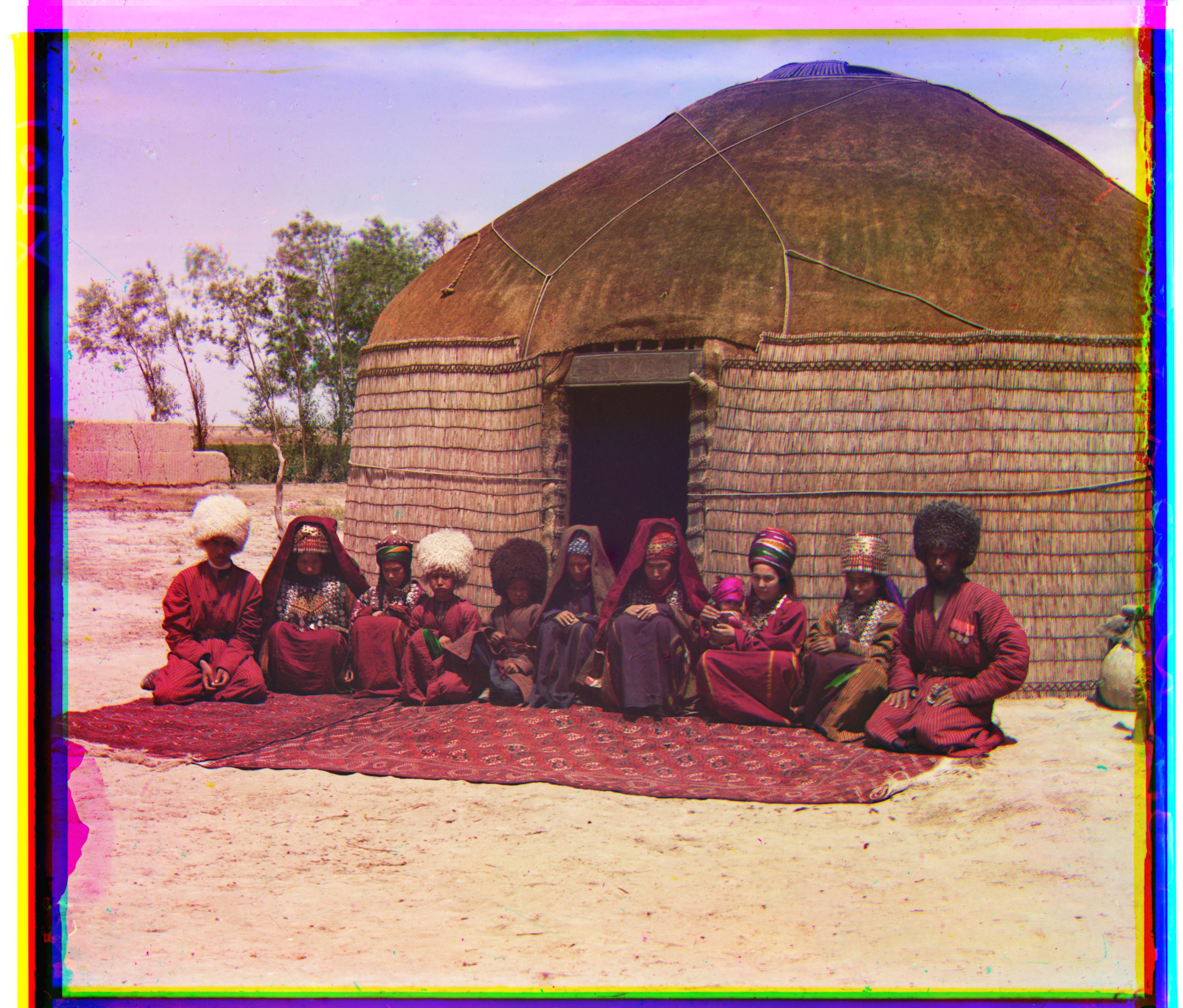 [Group of eleven adults and children, seated on a rug, in front of a yurt]